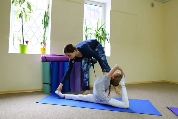 Little girl sits on twine and trainer helps child.