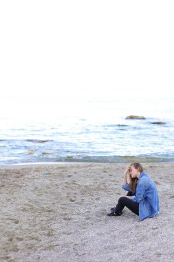 Gülümseyen genç kadın kumsalda aittir ve kamera, oturan pozlar