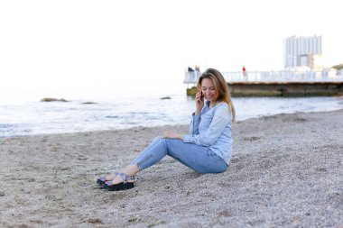 Güzel erkek mobil gülümseme ile konuşur ve plaj n üzerinde oturur