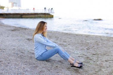 Gülümseyen genç kadın kumsalda aittir ve kamera, oturan pozlar
