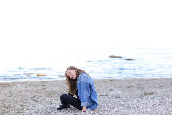 Sorridente giovane donna riposa sulla spiaggia e posa in macchina fotografica, seduta — Foto Stock