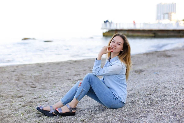 Улыбающаяся молодая женщина отдыхает на пляже и позирует перед камерой, сидя — стоковое фото