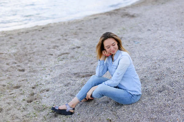 Gülümseyen genç kadın kumsalda aittir ve kamera, oturan pozlar — Stok fotoğraf