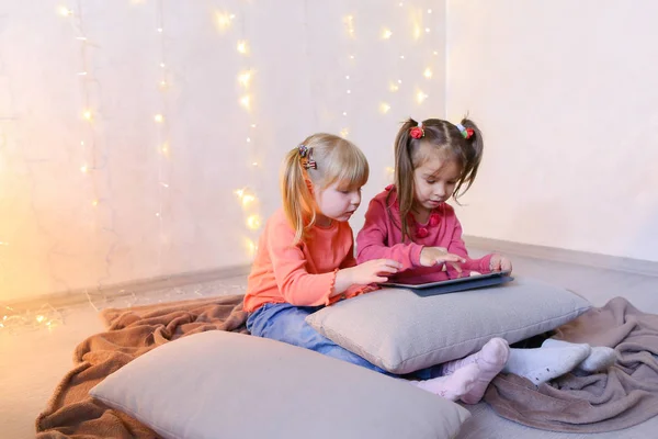 Little girls involved in use of tablet and sit on floor in brigh