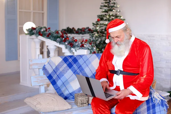 Jocund Father Christmas talking with video by laptop.