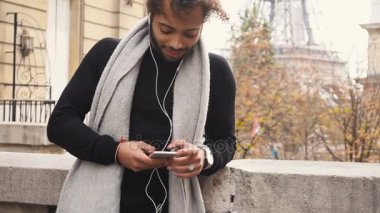 Genç erkek model smartphone ile sohbet ve Eyfel Kulesi yakınında müzik dinlemek.