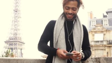 Melez erkek kişi tarafından smartphone ile kulaklık Eiffel tower yakınındaki arkadaşlarınızla sohbet.