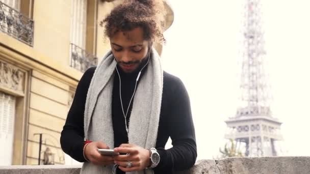 Meio menino nigeriano digitando mensagem e ouvindo música perto da torre Eiffel . — Vídeo de Stock