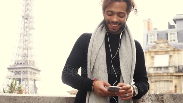 Mulat mężczyzna rozmawiać z przyjaciółmi przez smartphone rezygnować słuchawki w pobliżu Wieża Eiffla. — Wideo stockowe