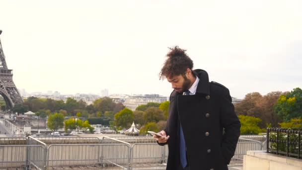 Niño árabe caminando cerca de la Torre Eiffel con smartphone en cámara lenta . — Vídeo de stock