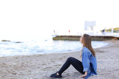 Gülümseyen genç kadın kumsalda aittir ve kamera, oturan pozlar