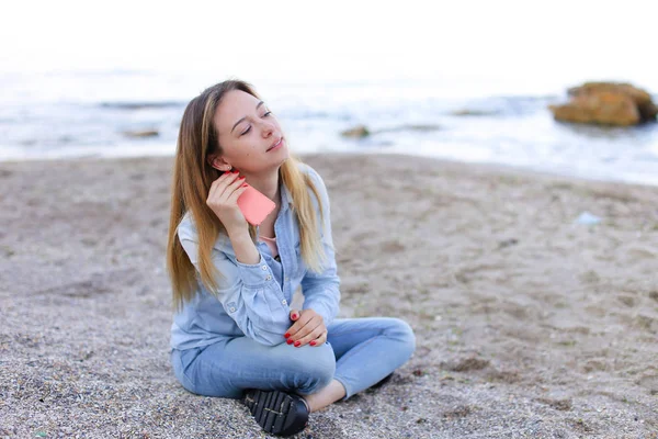 Härlig flicka chattare på telefon med leende och sitter på stranden n — Stockfoto