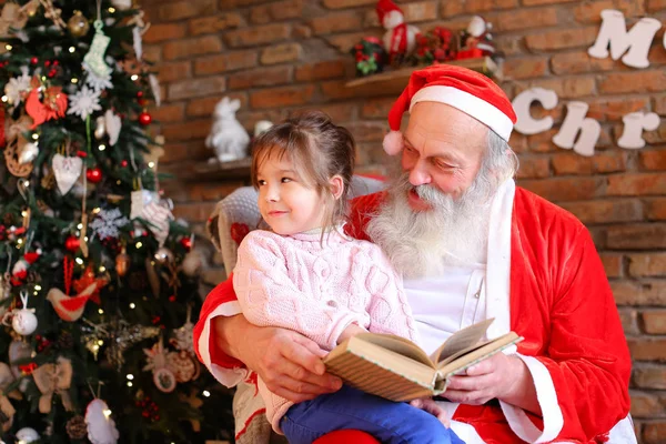 Santa Claus se sienta en el sillón y lee el libro con cuentos de hadas fo — Foto de Stock