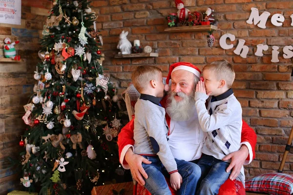 Two twin boys alternately make wish in ear of Santa Claus in de