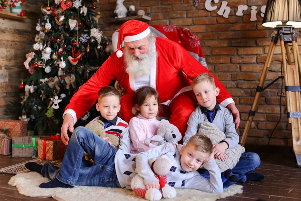 Geschwister sitzen neben Weihnachtsmännern, lächeln und lächeln. — Stockfoto