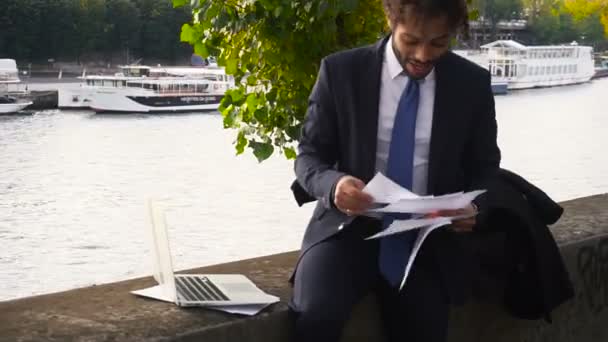 Mulat student čtení celoroční blízko řeky a práci s notebookem. — Stock video
