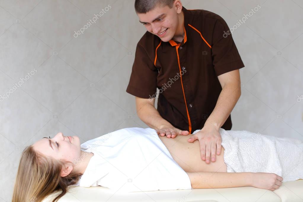 Strong male masseur with gentle hand movements kneads belly of c