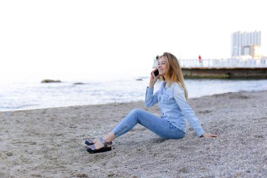 Güzel erkek mobil gülümseme ile konuşur ve plaj n üzerinde oturur