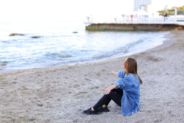 Hymyilevä nuori nainen lepää rannalla ja poseeraa kameran edessä, istuu — kuvapankkivalokuva