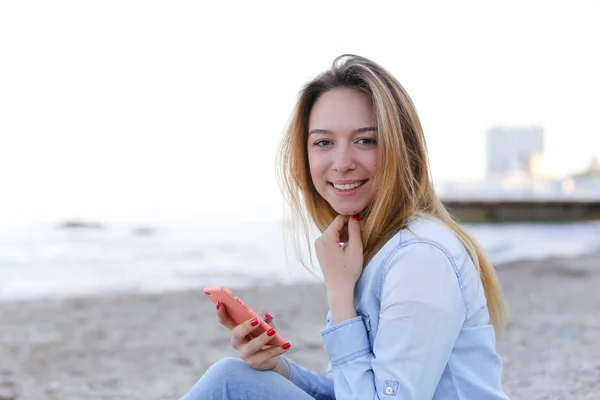 Mooi meisje chatters op telefoon met glimlach en zit op strand n — Stockfoto