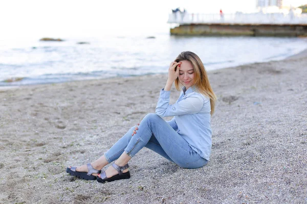 Gülümseyen genç kadın kumsalda aittir ve kamera, oturan pozlar — Stok fotoğraf