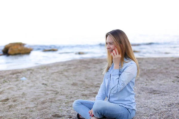 Mulher bonita fala no celular com sorriso e senta-se na praia n — Fotografia de Stock