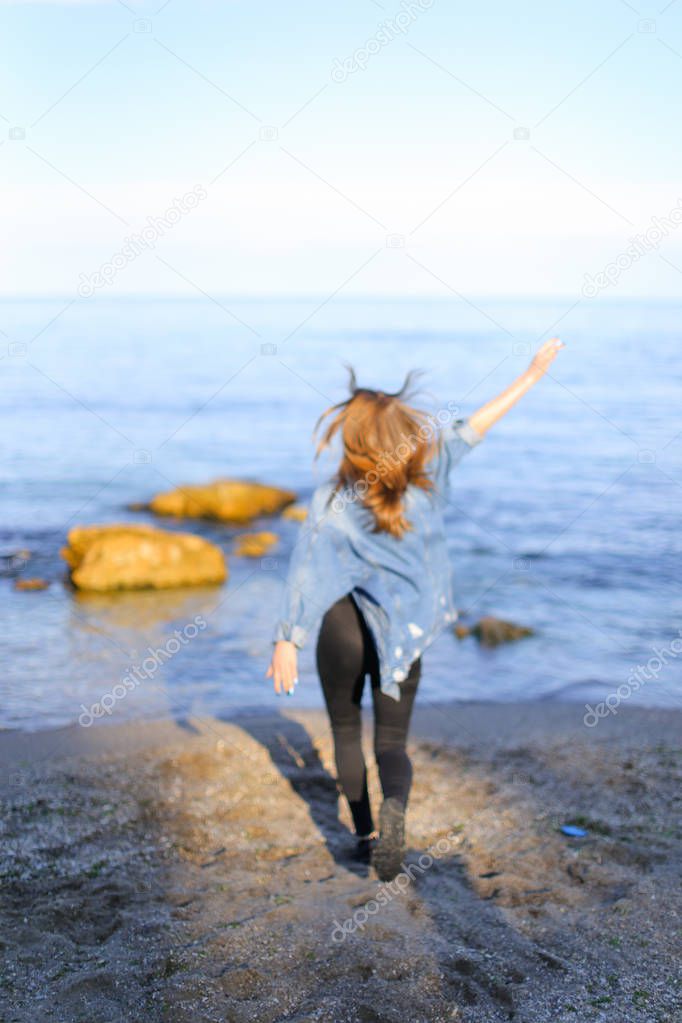 Charming girl walks along coast and merrily fools around on sand