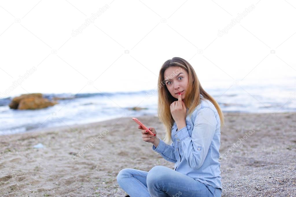 Lovely girl chatters on telephone with smile and sits on beach n