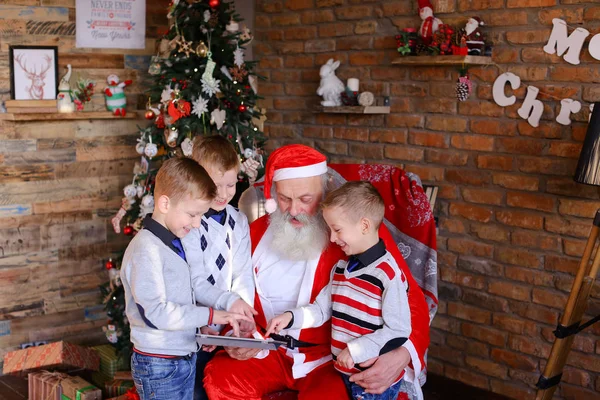 Los niños hermanos pequeños enseñan a Santa Claus a jugar en la tableta en el festival — Foto de Stock