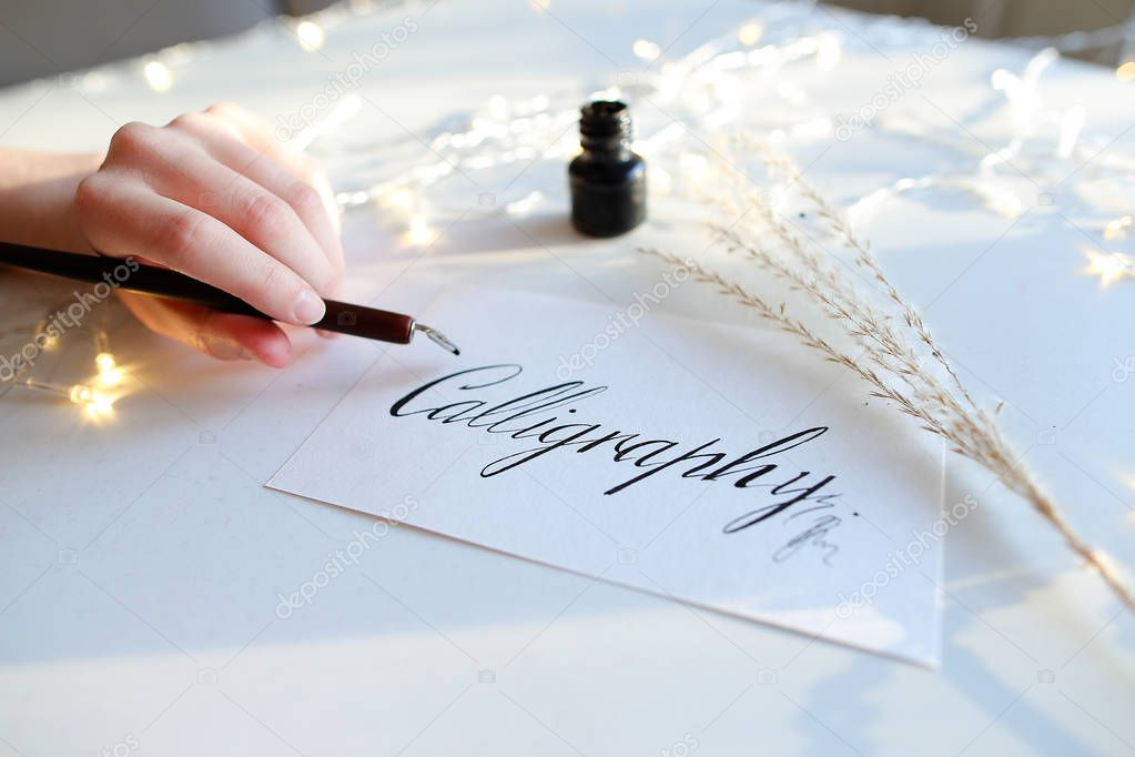 Female master of lettering of ink writes word on paper, sitting