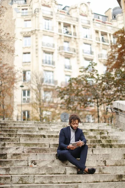 Mulatto businessman using tablet and sitting on steps. — Stock Photo, Image