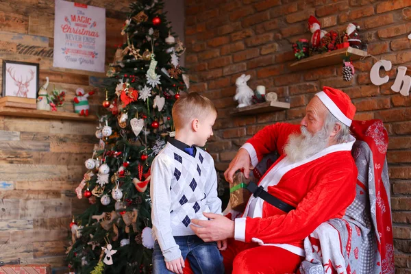 Niño pequeño corre a Santa Claus, se sienta de rodillas y pide deseo , — Foto de Stock