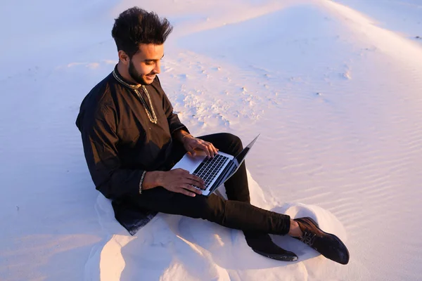 英俊的年轻阿拉伯男子写在互联网使用的便携式计算机上并坐 — 图库照片