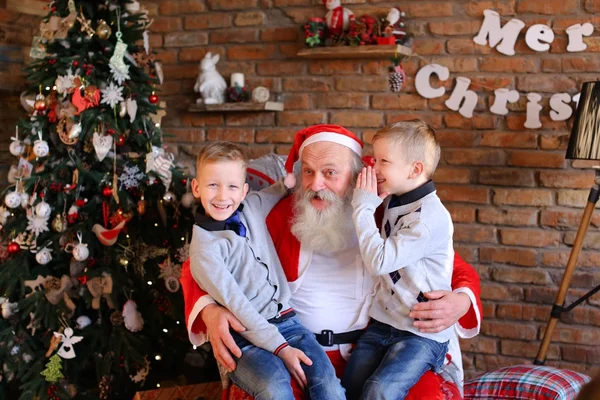 Dos chicos gemelos alternativamente pedir deseo en la oreja de Santa Claus en de — Foto de Stock