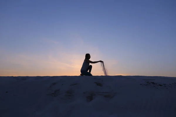 Belle fille est assise à s'accroupir sur une colline sablonneuse du désert au coucher du soleil — Photo