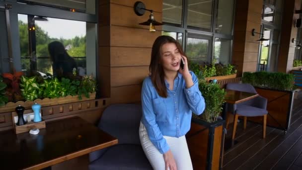 Hübsches Mädchen sitzt im Sessel und spricht per Smartphone im Restaurant in Zeitlupe. — Stockvideo