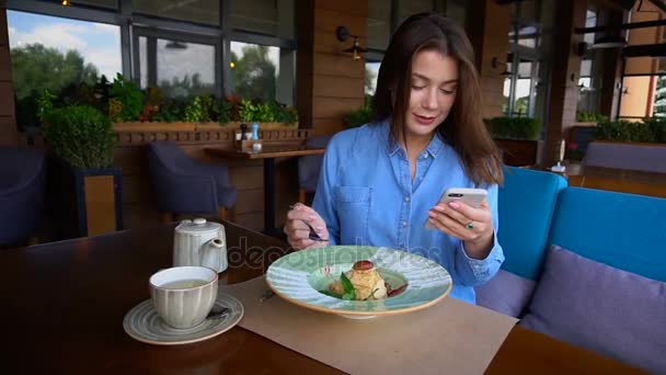 Mujer bonita sentada en la cafetería, charlando por teléfono inteligente y tomando postre en cámara lenta . — Vídeo de stock