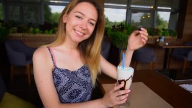 Dondurma kokteyl ile kafede oturan ve kamera yavaş çekimde bakarak neşeli kız.