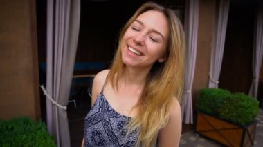 Kameraya bakarak ve yüz kadar yakın kafe yakınındaki ağır çekimde gülümseyen genç kadın.