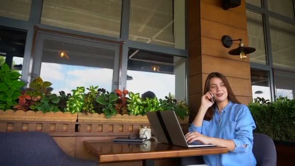 Freelancer pratar av smartphone och arbetar med laptop på café. — Stockvideo