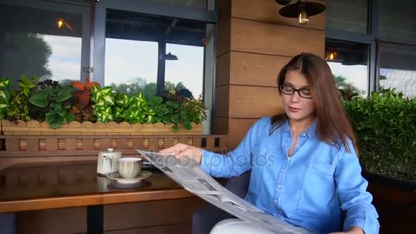 Menina bonita sentada na cadeira braço restaurante e ler artigos de jornal em câmera lenta . — Vídeo de Stock