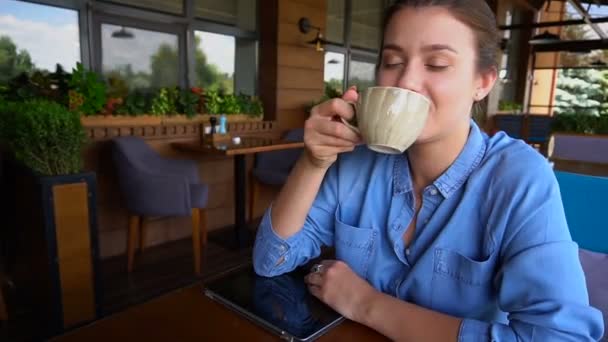 Gladden persona femenina beber té y sentarse en el restaurante con la tableta en cámara lenta . — Vídeos de Stock