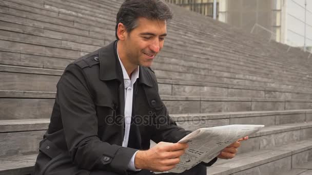 Slow motion male business tutor sitting on stairs and reading newspapers. — Stock Video