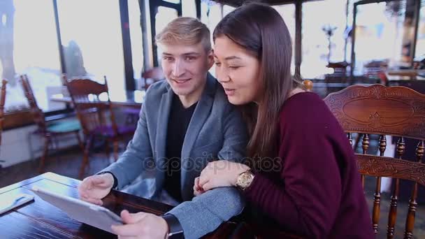 Garçon et fille assis à la table de café avec tablette et rire . — Video