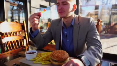 Fast food yeme keyfini akıllı saatle gri ceket giymiş işadamı.