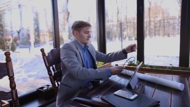 Ingeniero joven esperando antes de la entrevista de trabajo con la tableta, teléfono inteligente, auriculares y proyecto — Vídeo de stock