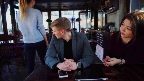 Girlfriend and boyfriend wear smartwatch on hand sitting near table with smartphone and laptop quarrel. — Stock Video