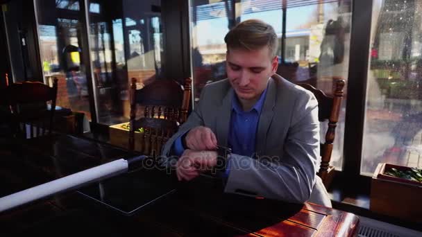 Студент використовує розумний годинник і сидить у кафе з рулонним проектом, планшет на столі . — стокове відео