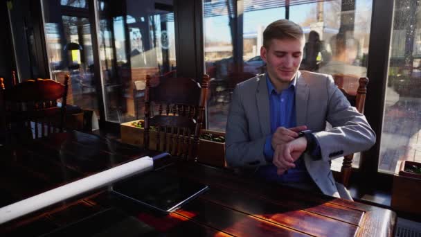 Projektant wnętrz, siedząc w kawiarni, przy użyciu inteligentny zegarek w pobliżu projekt rolki i smartphone. — Wideo stockowe