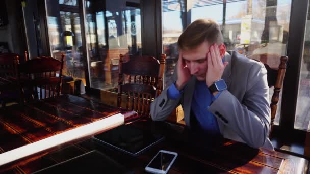 Joven gerente cansado teniendo descanso en la cafetería con rollo de papel, tableta y teléfono inteligente en la mesa . — Vídeos de Stock